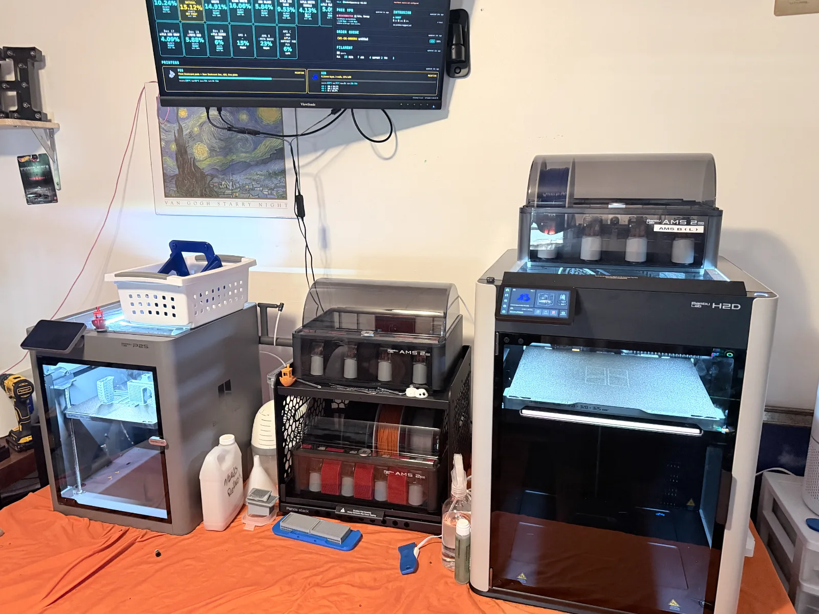 The BrokenITguy CustomWorks workshop in Knoxville — a Bambu Lab P2S and H2D printing side by side with AMS units and a live monitoring dashboard on the wall